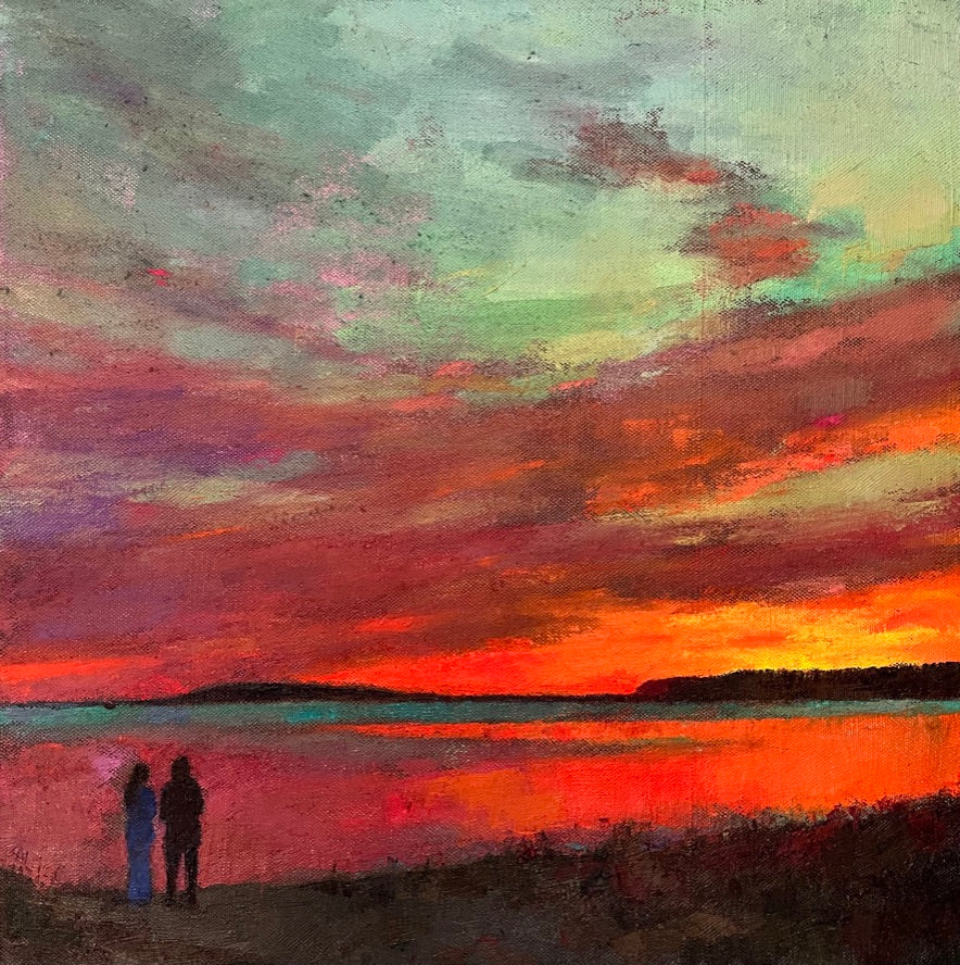 Deep red, orange and pink reflect upon the water. Two figures stand admiring the sunset