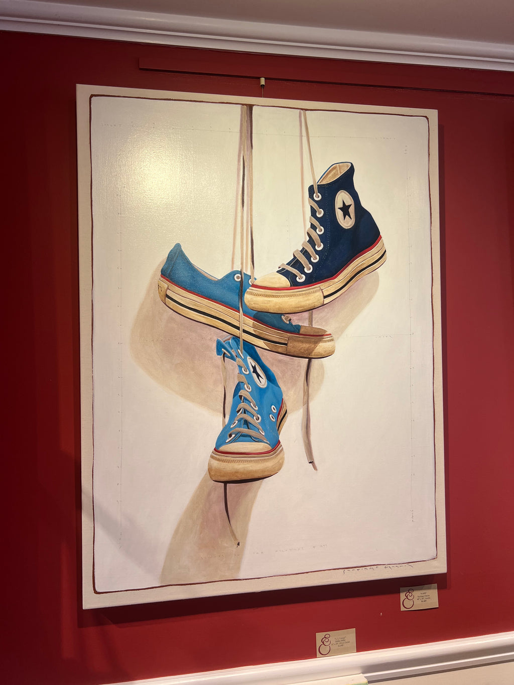 oil painting of converse sneakers in three shades of blue hanging by laces 